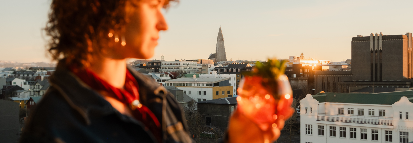 Person holding a cocktail with Reykjavík skyline and Hallgrímskirkja at sunset