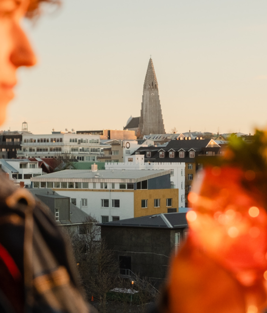 Person holding a cocktail with Reykjavík skyline and Hallgrímskirkja at sunset