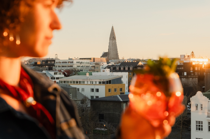 Person holding a cocktail with Reykjavík skyline and Hallgrímskirkja at sunset