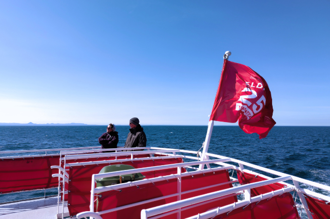 Visitors enjoying a whale watching tour on a boat in Reykjavík Bay with an Elding flag and ocean views