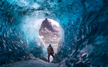 Person standing at the entrance of a bright blue ice cave in Iceland during winter.