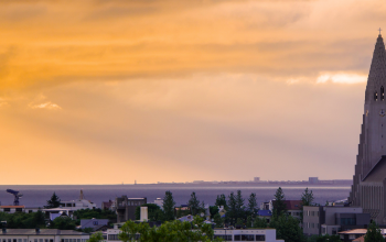 Hallgrímskirkja church rising above Reykjavík skyline at sunset with orange sky and the ocean in the background.