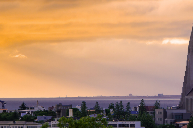 Hallgrímskirkja church rising above Reykjavík skyline at sunset with orange sky and the ocean in the background.