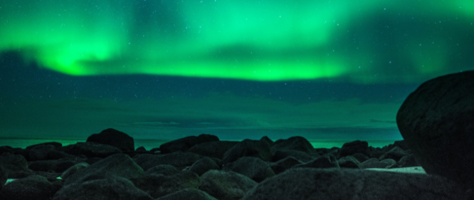 Green aurora lighting up the night sky above a rocky shoreline in Iceland.