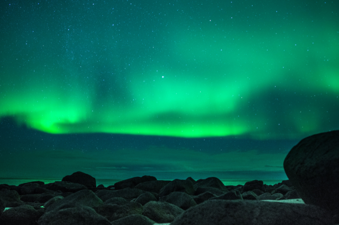 Green aurora lighting up the night sky above a rocky shoreline in Iceland.