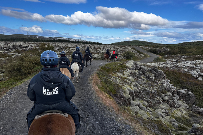 Horseback riders exploring a trail through Icelandic lava fields under a blue sky.