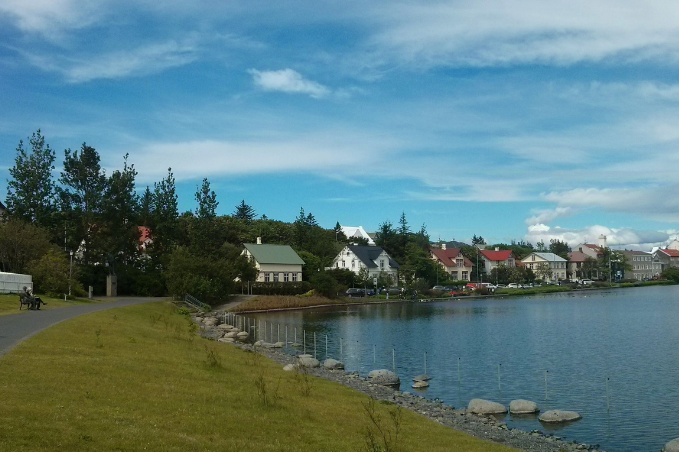 Walking path along Tjörnin Pond with trees and colorful houses in central Reykjavík.