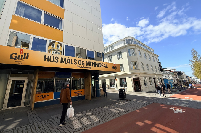 Yellow storefront of Hús Máls og Menningar bookshop on Laugavegur, with pedestrians walking through central Reykjavík.