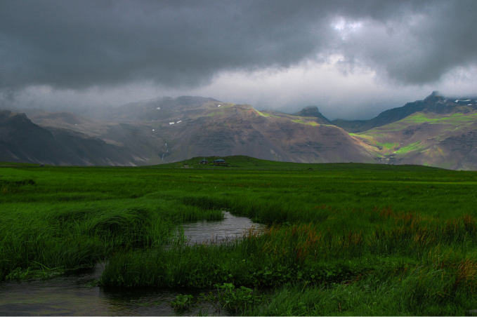 Green wetlands beneath dark clouds and mountains in snaefellsnes peninsula.