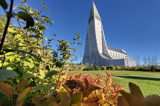 Hallgrímskirkja rising above autumn gardens under a clear blue sky.
