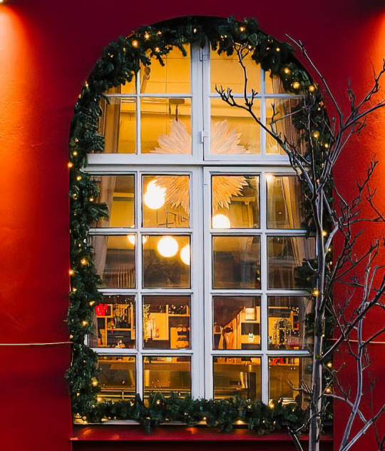 Warmly lit restaurant windows decorated with Christmas lights and garlands on a red building in Reykjavík.