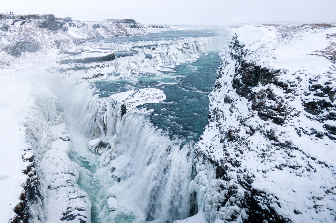 A picture of the Gullfoss waterfall that is a part of the Golden circle tour in Iceland with blue water and snow covered rocks around.