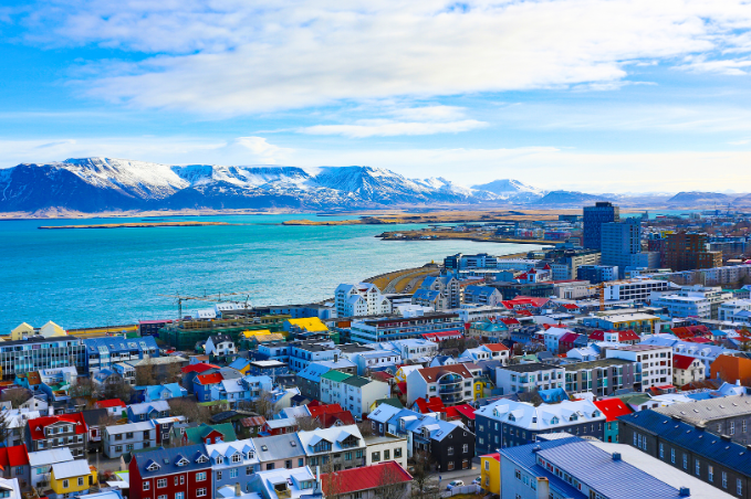 Panoramic view of Reykjavik with colorful rooftops, the ocean, and snow-capped mountains in the back.