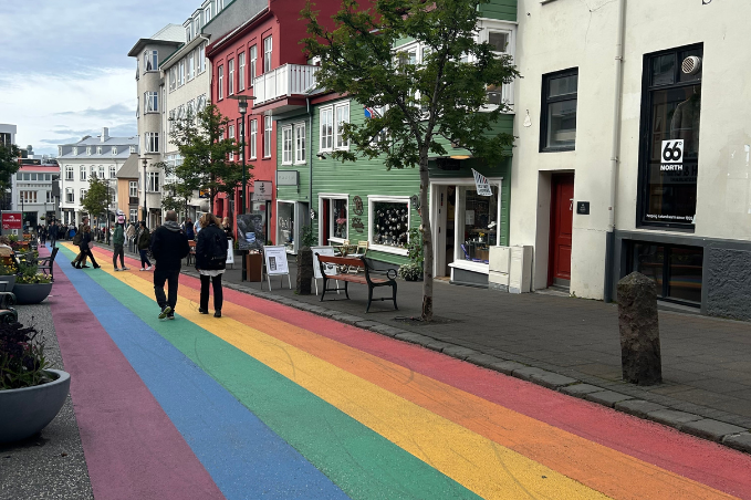 Colorful rainbow-painted street with pedestrians and small shops in downtown Reykjavik.