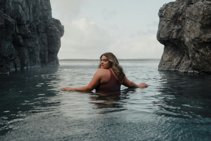 Woman relaxing in Sky Lagoon in Iceland surrounded by dark volcanic rock cliffs.