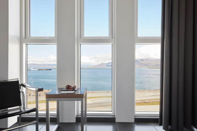 Large windows in a sea view room at Center Hotels Arnarhvoll in Reykjavik overlooking the city's waterfront and mountains in the distance.
