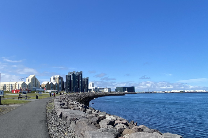 Coastal walking path along Reykjavík's waterfront with modern buildings and calm sea.