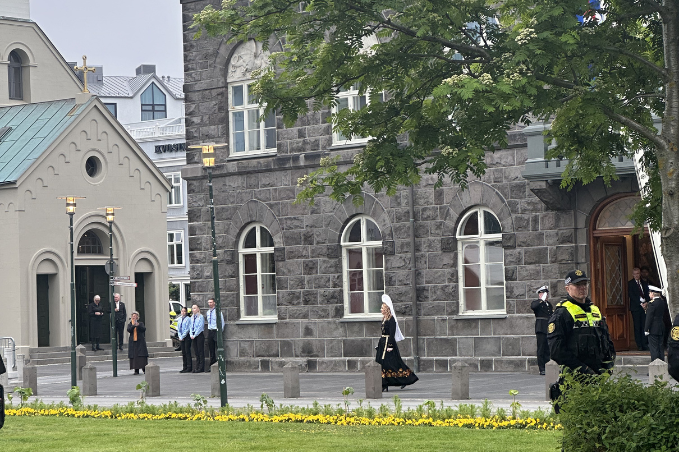 Woman in traditional Icelandic national costume walking outside Alþingi Parliament House in central Reykjavík with police and visitors nearby.