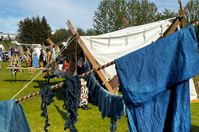 Traditional blue-dyed textiles hanging at an outdoor medieval festival with historical reenactors and market tents in Hafnarfjordur.
