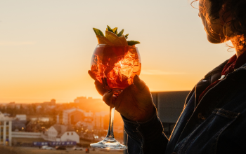 Guest holding a colorful cocktail while enjoying panoramic sunset views over Reykjavík from a rooftop bar.