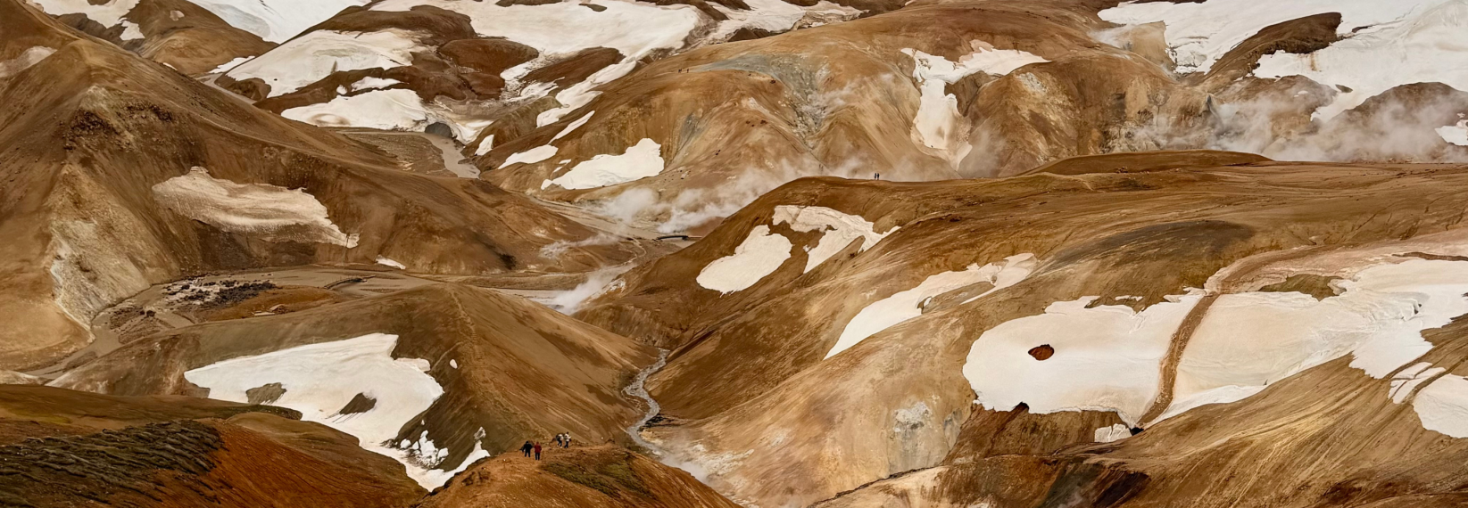 Panoramic view of the colorful rhyolite mountains, geothermal steam vents, snow patches, and hiking trails in Landmannalaugar, Iceland.