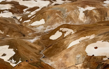 Panoramic view of the colorful rhyolite mountains, geothermal steam vents, snow patches, and hiking trails in Landmannalaugar, Iceland.