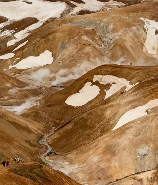 Panoramic view of the colorful rhyolite mountains, geothermal steam vents, snow patches, and hiking trails in Landmannalaugar, Iceland.