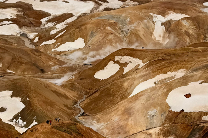 Panoramic view of the colorful rhyolite mountains, geothermal steam vents, snow patches, and hiking trails in Landmannalaugar, Iceland.