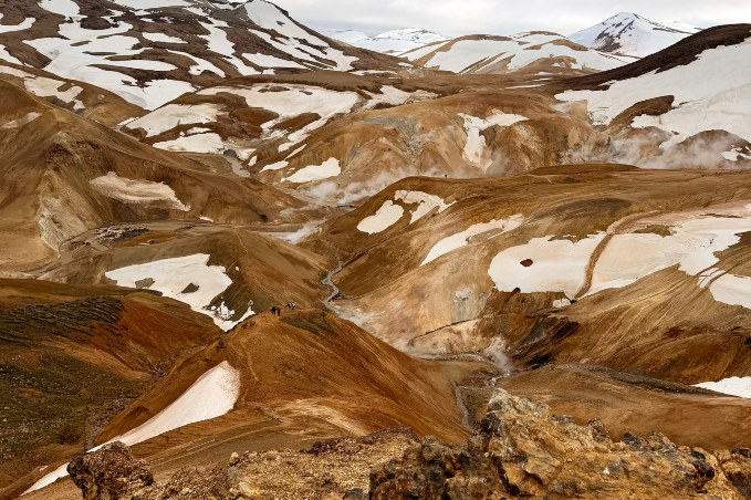 Wide landscape of Landmannalaugar featuring colorful volcanic mountains, steaming geothermal valleys, melting snow, and hiking paths in Iceland's Highlands.