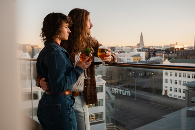Couple enjoying drinks on a rooftop terrace overlooking downtown Reykjavík and Hallgrímskirkja.