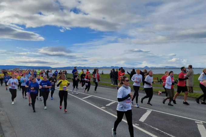 Runners taking part in the Reykjavík Marathon along the waterfront with mountains in the distance.