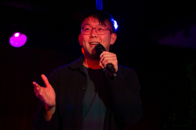 Stand-up comedian performing on stage with a microphone under colorful lights in Reykjavík.