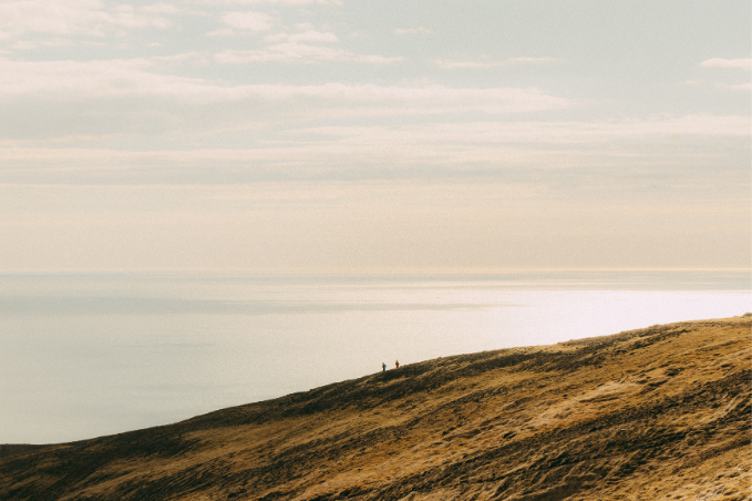 Hikers on a grassy slope of Mount Esja overlooking the sea in soft evening light.