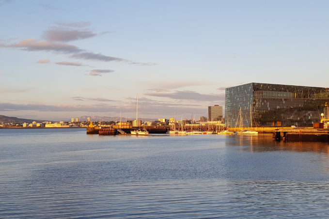 Harpa Concert Hall and moored ships at Reykjavík harbour, with golden sunlight reflecting on the calm water.