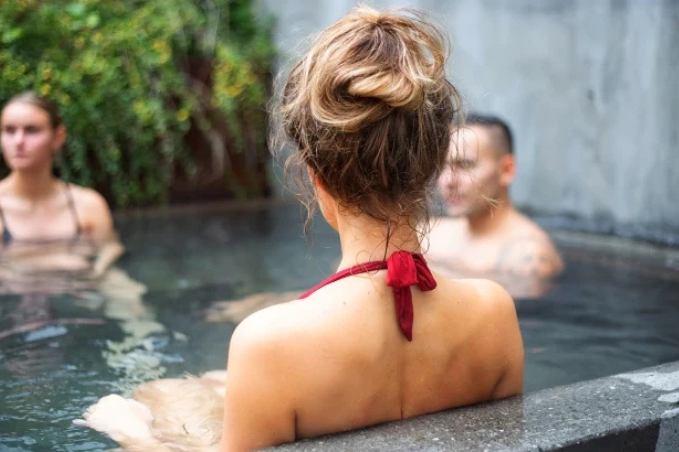 Guests relaxing in the outdoor hot tub at Miðgarður Spa in Reykjavík, surrounded by greenery and concrete walls.