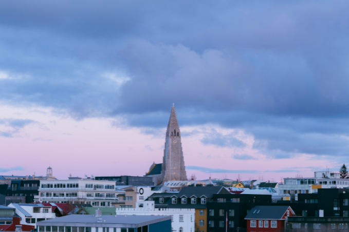 Hallgrímskirkja rising above Reykjavík’s colourful rooftops beneath a pink and blue sky with dramatic clouds.
