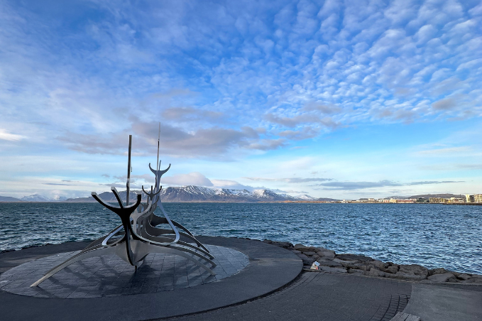 Sun Voyager sculpture on Reykjavík’s waterfront, with the sea and snow-capped mountains beneath a blue, cloud-filled sky.