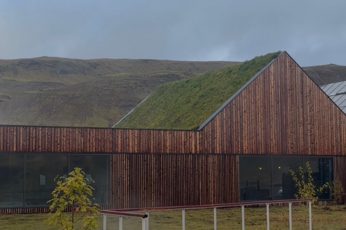 Timber-clad spa building with a sloping turf roof, large windows and a gently sloping access ramp, backed by grassy hills.