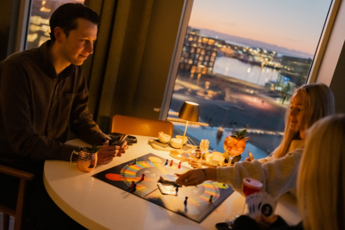 Friends playing a board game with cocktails in SKÝ loung and bar overlooking the city