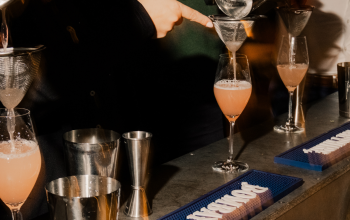 Bartenders preparing pink craft cocktails behind a bar in Reykjavík, Iceland, with cocktail strainers, glassware, and a lively evening atmosphere.