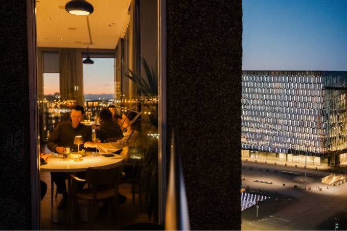 Guests enjoying evening drinks in a Reykjavík hotel room overlooking Harpa Concert Hall