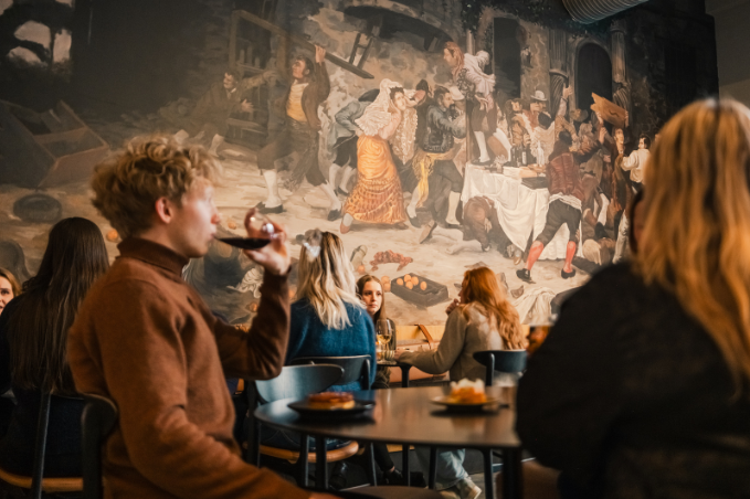 Guests relaxing with wine inside Grandi restaurant and bar featuring a large historic inspired mural
