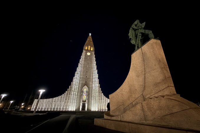 Hallgrímskirkja church illuminated at night beside the Leif Erikson statue in Reykjavík