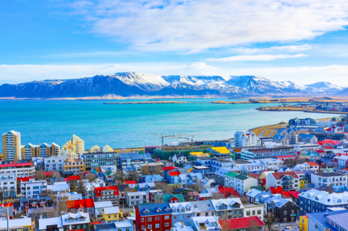 Panoramic view of Reykjavik with colorful rooftops, the ocean, and snow-capped mountains.