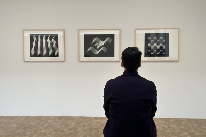 Person sitting on a bench viewing black-and-white abstract artworks in a museum gallery.