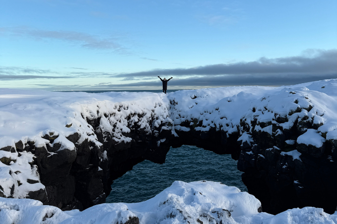 Person standing on a snowy rock arch by the ocean in Iceland