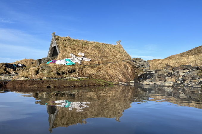 Old Icelandic turf house reflected in calm water under a clear sky