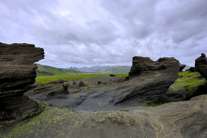 Dark volcanic rock formations in a wide Icelandic valley under cloudy skies