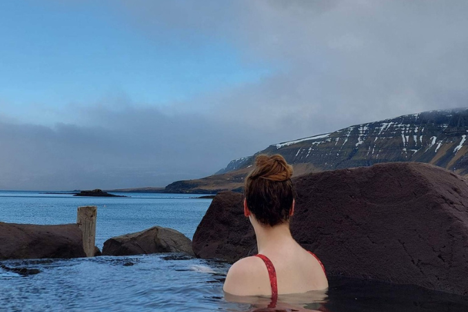 Guest relaxing in Hvammsvik Hot Springs surrounded by mountains and ocean views in Iceland