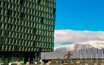 Glass facade of Harpa Concert Hall in Reykjavik with snowy Mount Esja in the background on a bright winter day.